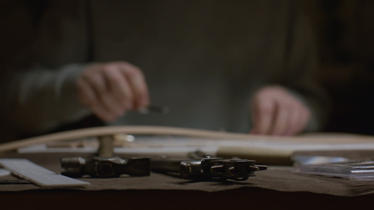 Leatherworking tools, including a hammer and hole punch, rest on a workbench while an artisan works in the background.