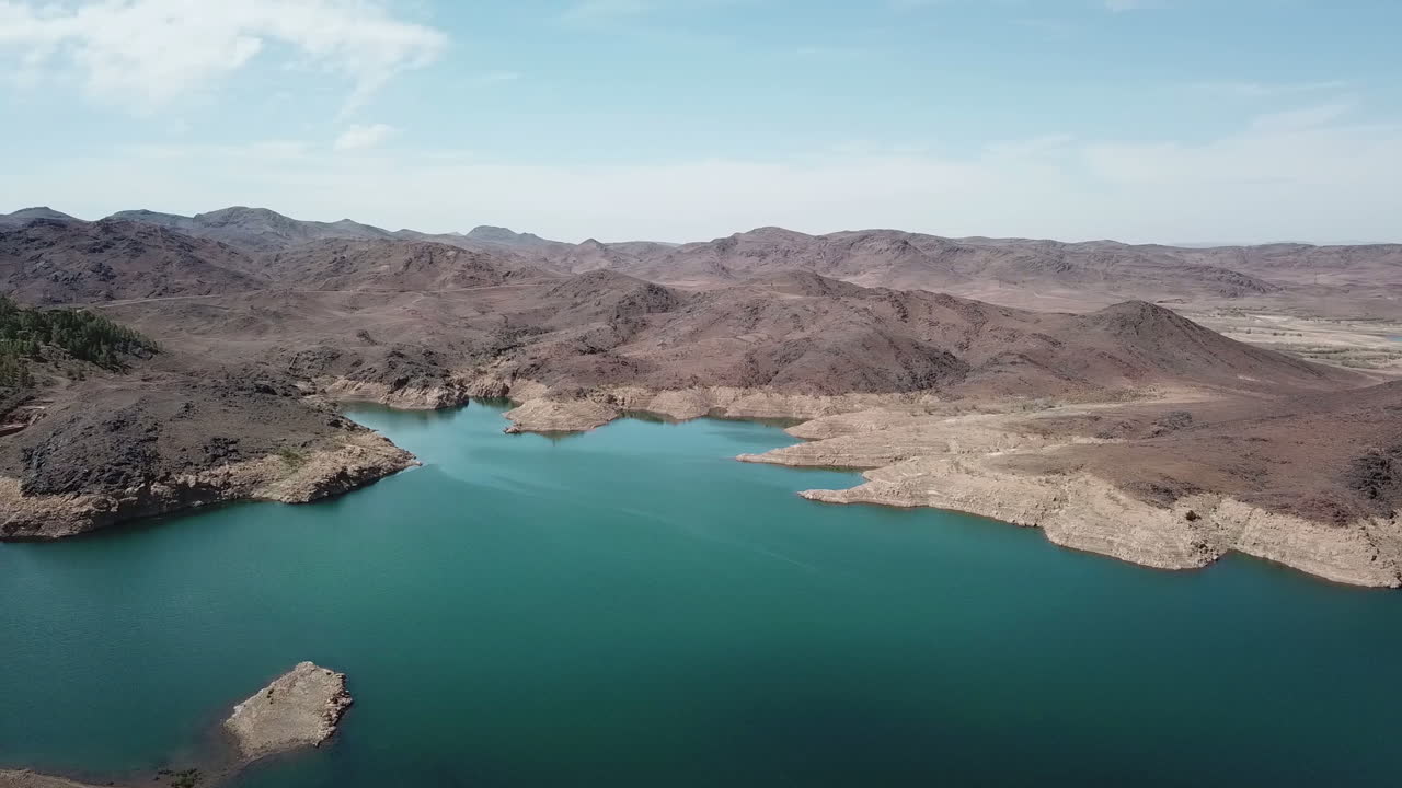 Ripresa aerea cinematografica in 4K di uno splendido lago-serbatoio blu turchese incastonato in un canyon aspro e arido. L'inquadratura mostra il bellissimo contrasto tra acqua profonda e montagne desertiche e secche.