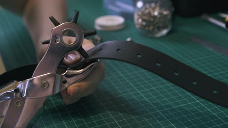 professional tailor makes holes in belt with punch pliers