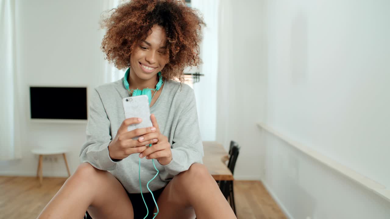 una hermosa joven afroamericana enviando mensajes de texto por teléfono móvil en casa.
