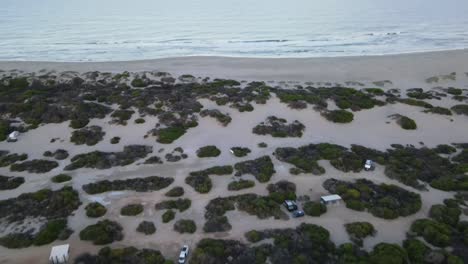 Drone-aerial-panning-up-from-a-beach-side-camping-spot-to-a-pristine-beach-during-sunrise