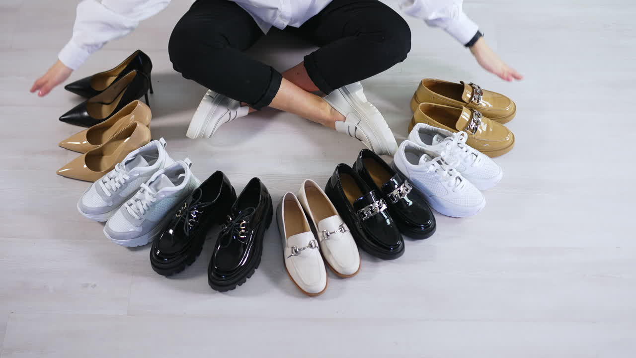 Woman sitting on the floor counts the pairs of shoes in front of her. Variety of footwear presentation. View from top.