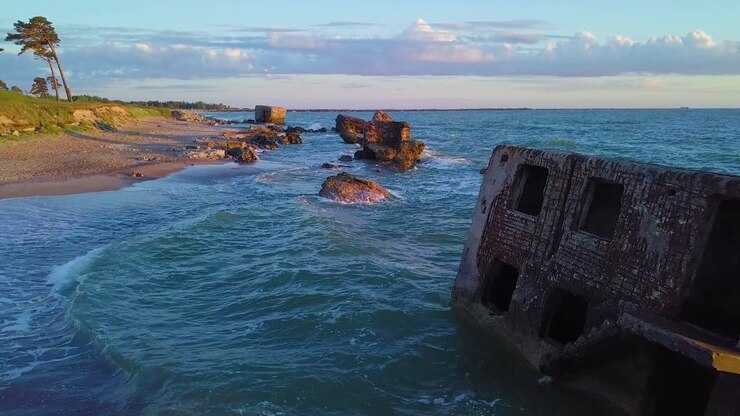 Aerial view of abandoned seaside fortification buildings at Karosta Northern Forts on the beach of Baltic sea , waves splash, golden hour sunset, wide drone shot moving forward