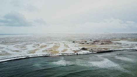 aerial shot pulling back from sandgerdi iceland with small cottages dotting the coast and white capped waves hitting the shore