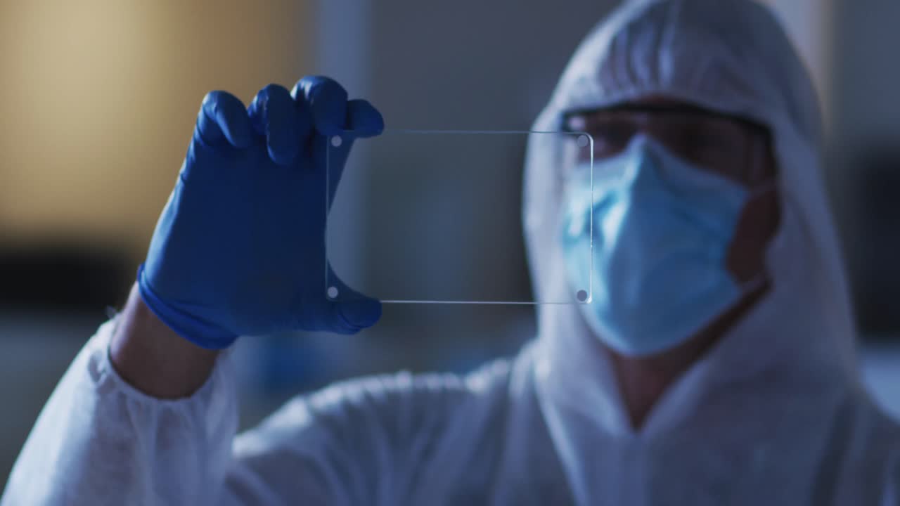 Caucasian male medical worker wearing protective clothing and gloves using handheld interface in lab