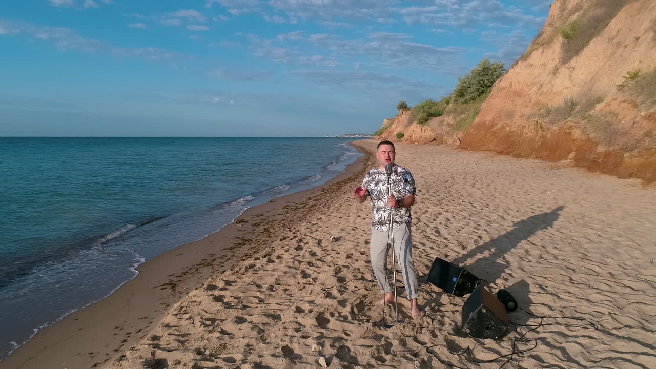 Man singing into microphone outdoor. Young man singing into microphone while standing on the beach