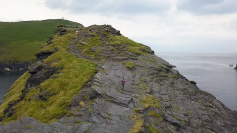 hiker climbing and ascending rocky coastal headland cliff, cornwall uk, aerial