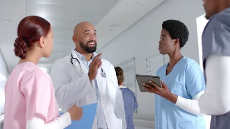 diverse doctors discussing work and using tablet in corridor at hospital, slow motion