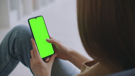 punto de vista de la mujer en una habitación moderna sentada en una silla usando un teléfono con pantalla de maqueta verde clave de croma navegando por internet viendo videos de contenido blogs tocando en la pantalla central