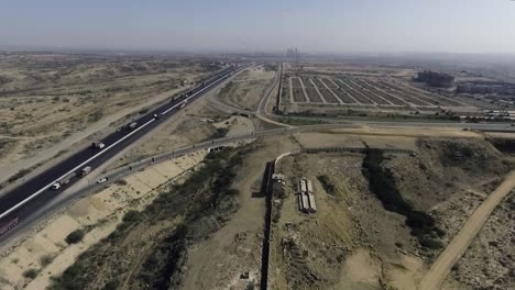an aerial slow mo view of a highway and city, the heavy trawlers and cars are moving on the highway, an interchange is connecting