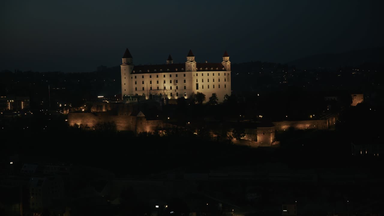 Bratislava Castle glowing at night with warm lights and dark hills in the background
