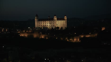 bratislava castle glowing at night with warm lights and dark hills in the background