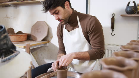 young man wearing apron working at pottery wheel in ceramics studio