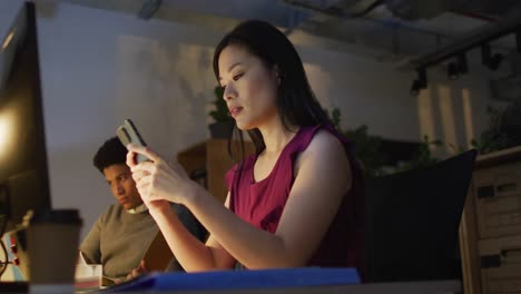 Video-De-Una-Mujer-Asiática-Usando-Un-Teléfono-Inteligente,-Trabajando-Hasta-Tarde-En-La-Oficina