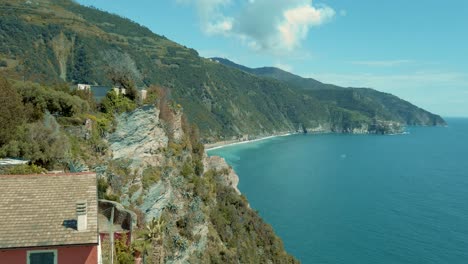 Vista-Panorámica-De-Cinque-Terre-Corniglia-Que-Revela-El-Mar-Entre-Casas,-Costa,-Nubes,-Horizonte,-Vacaciones,-Chimenea,-Cielo-Azul,-Italia