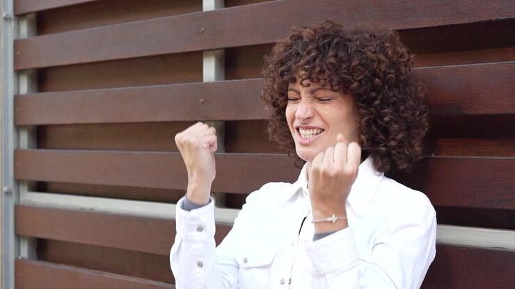Una donna elegante con bellissimi capelli ricci posa elegantemente su uno sfondo urbano moderno.