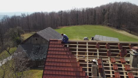 drone shot van een man die dakpannen installeert op een huis op het platteland