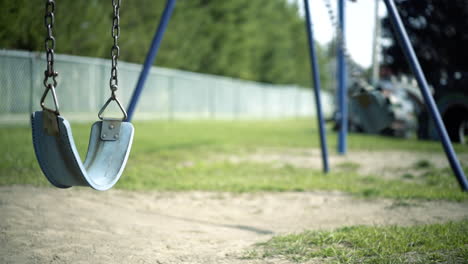 abandoned empty swing set swings swaying in wind at children's playground with fenceline in background during summer time second swing is moving faster 4k prores