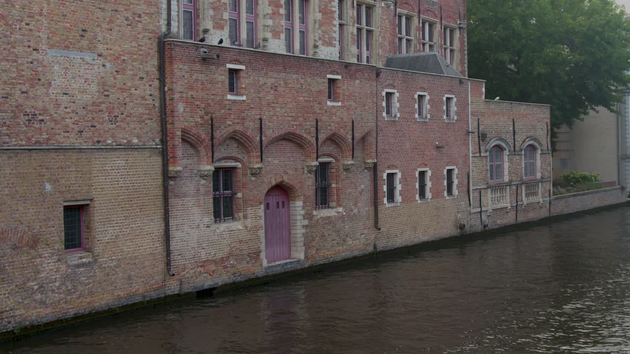 Camera pans along historic red brick building beside canal, overcast daylight, tranquil atmosphere