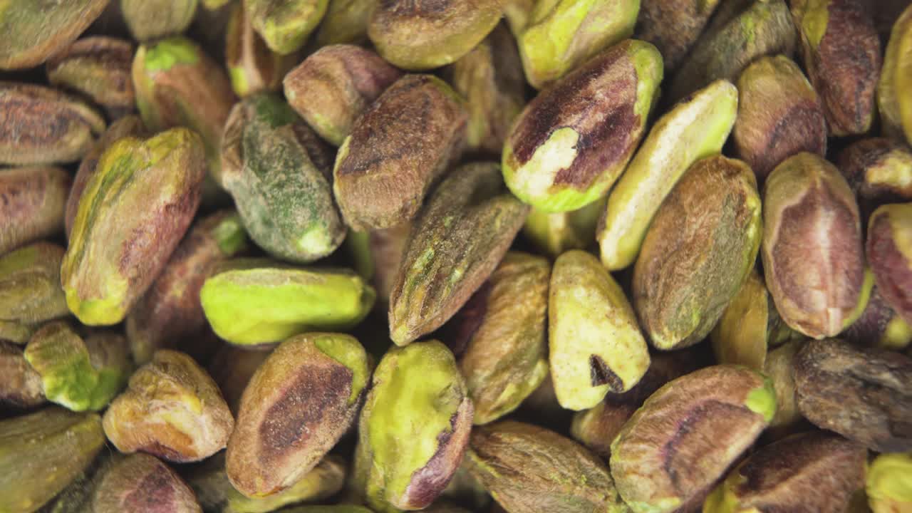 A beautifully detailed macro shot of raw pistachio nuts without shells, captured from a top-down angle. The natural green tones and textures of the pistachios are highlighted in soft light