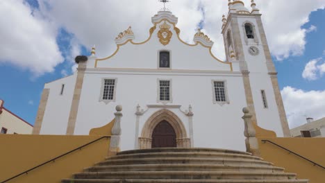 white facade of portimao parish church with stork nest, clock tower and golden details under partially cloudy sky