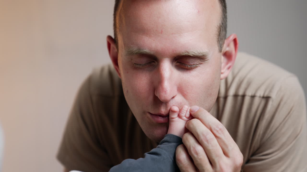 Caucasian man kisses tenderly tiny infant's foot. Happy father with his beloved newborn. Close up.