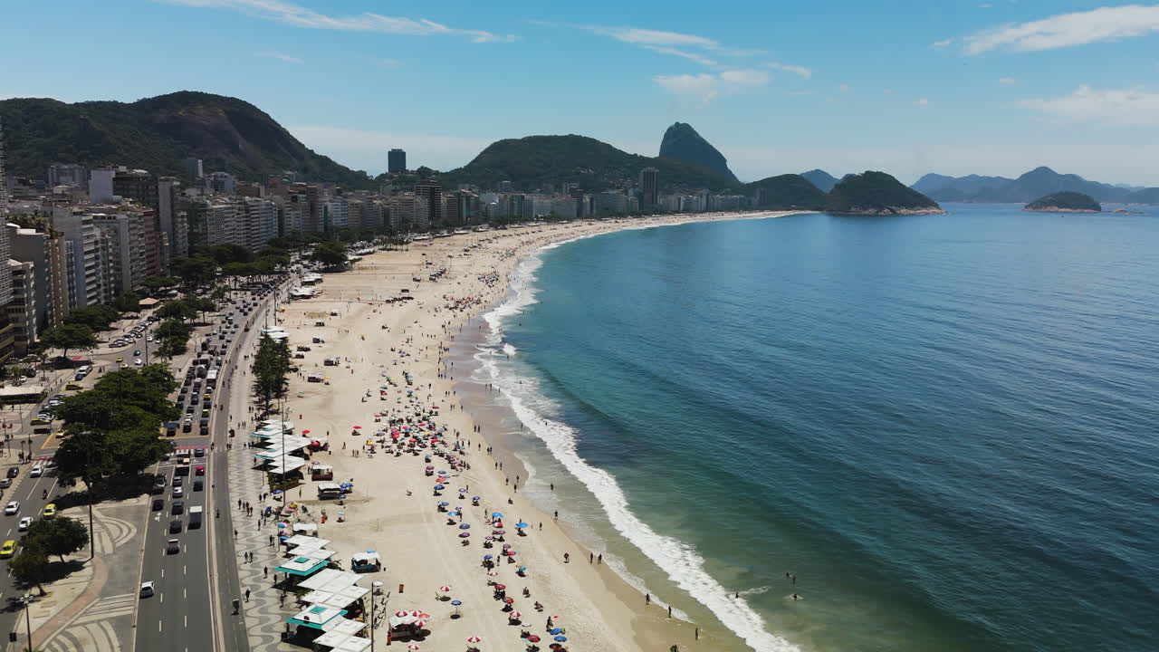Drone descends over sunny Copacabana Beach with Sugarloaf Mountain towering behind