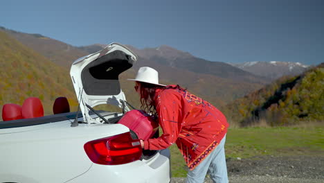 woman packing suitcase in convertible car trunk, mountain view