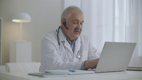 online appointment with pediatrician or therapist male doctor is working remotely from his office using laptop with video calling