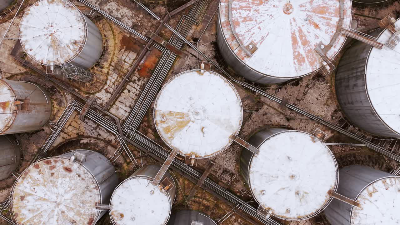 Rotating aerial perspective captures grid of storage tanks and weathered pipes