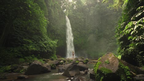 Mujer-De-Viaje-Rubia-En-Forma-Pisando-Roca-En-La-Impresionante-Cascada-De-Nungnung