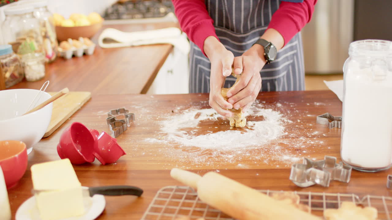 Biracial man wearing christmas hat, making christmas cookies in kitchen at home, slow motion