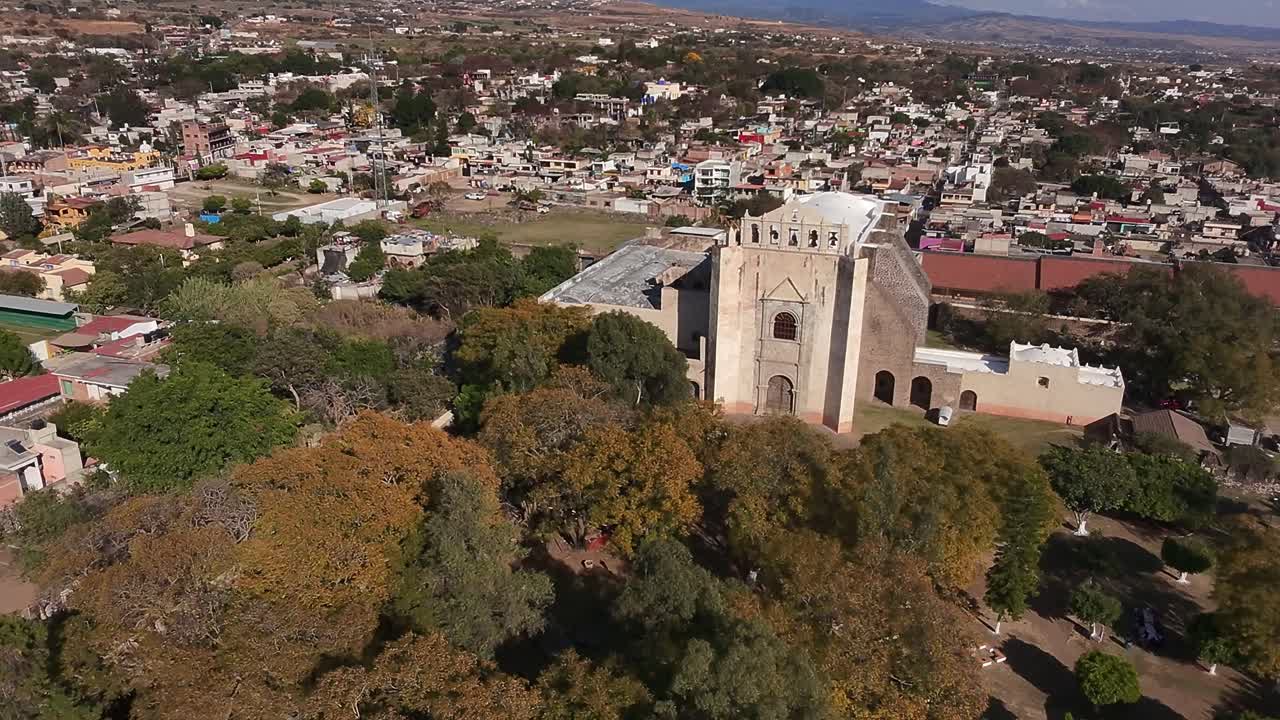 Drone shot of colonial church and townscape near Oaxtepec and Tlayacapan, Morelos. Large stone church surrounded by trees with colorful town buildings in the background