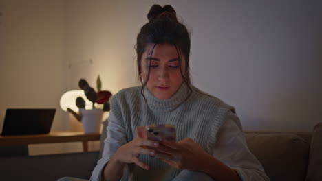 mujer gamer leyendo teléfono inteligente poniendo gamepad en el sofá por la noche en casa closeup