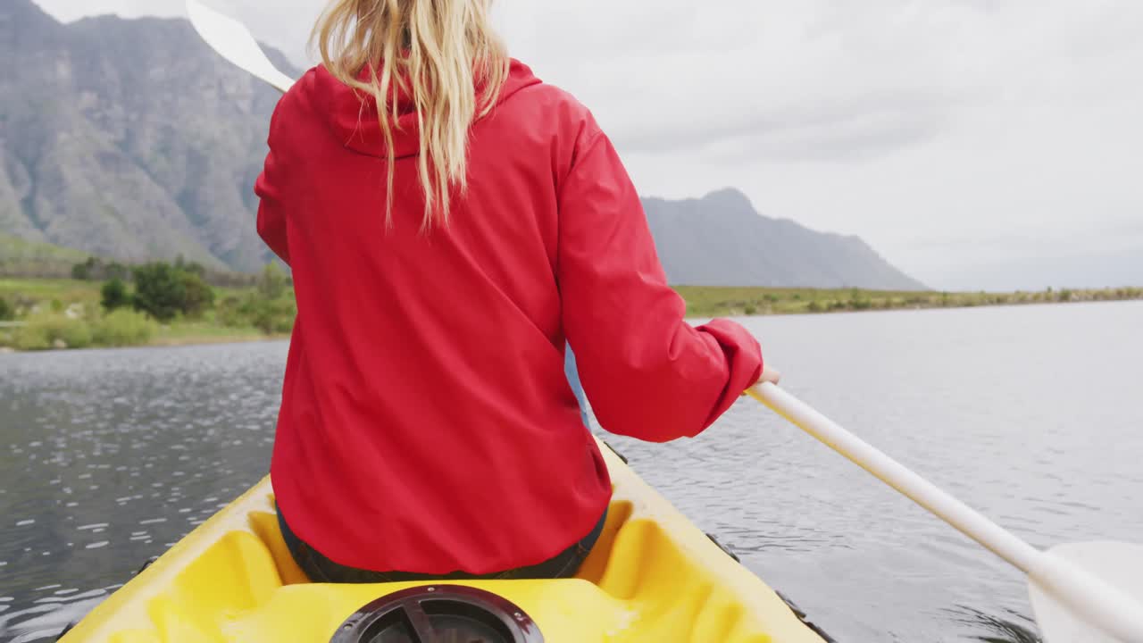 Caucasian woman having a good time on a trip to the mountains, kayaking on a lake, holding a paddle