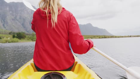 caucasian woman having a good time on a trip to the mountains, kayaking on a lake, holding a paddle