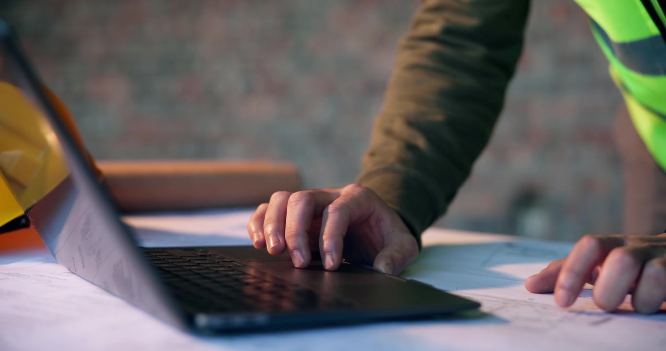 Construction Engineer Using Laptop Over Blueprints at Site