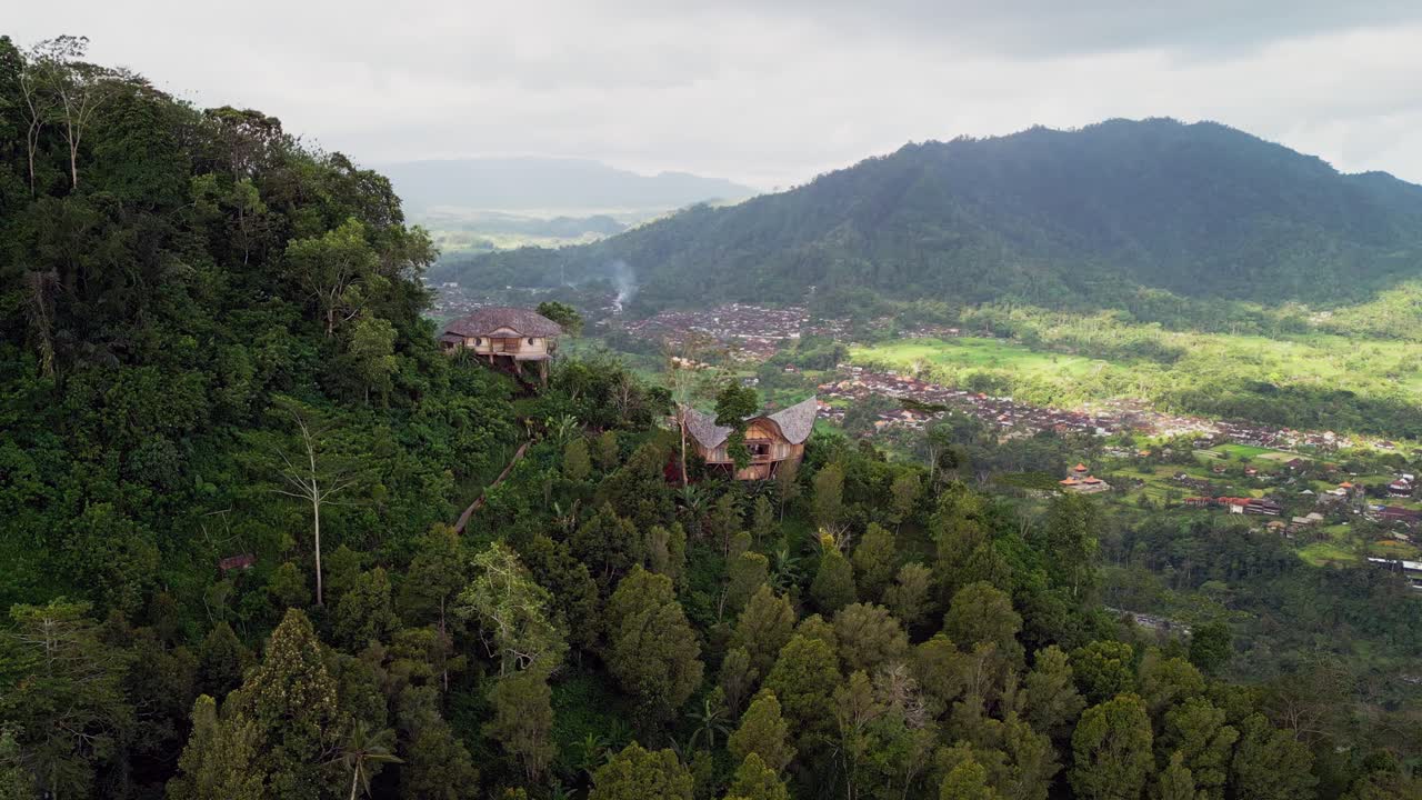 Drone footage capturing bamboo villas on lush mountainsides of Sidemen Bali. Green valleys, rice terraces, and forest views highlight a tranquil luxury retreat surrounded by nature and culture
