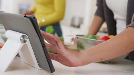 Midsection-of-biracial-sisters-cooking-dinner-together-and-using-tablet-in-kitchen,-in-slow-motion