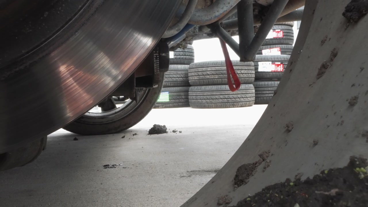 Person Walks with Red Jerry Can Past Car Wheel and Stacked Tires