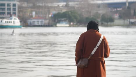 woman wearing hijab and coat walking by the sea in istanbul