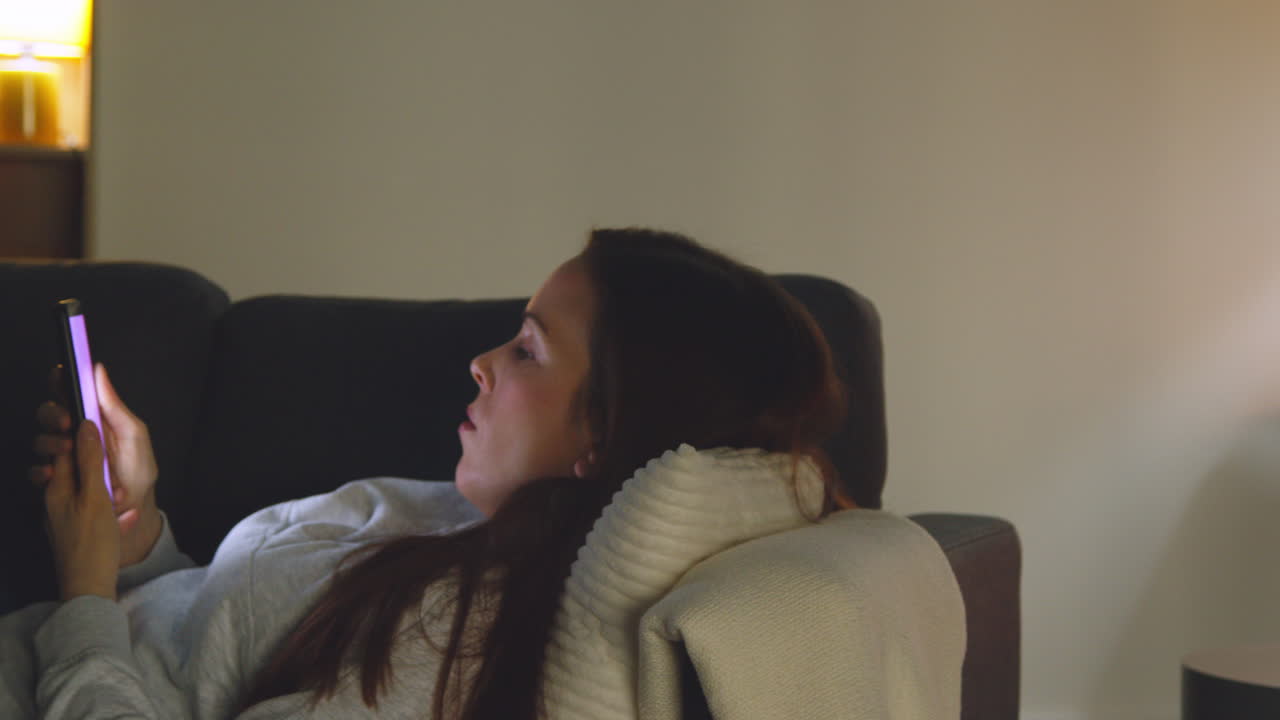 밤에 집에서 소파에 누워서 휴대 전화로 온라인 콘텐츠를 스트리밍하거나 보는 여성 5