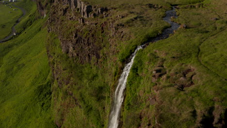 Orbit-overhead-drone-view-of-majestic-Seljalandsfoss-waterfall-in-Iceland,-most-famous-travel-destination.-Top-down-view-of-water-flowing-over-green-mossy-cliffs.-Beauty-on-earth