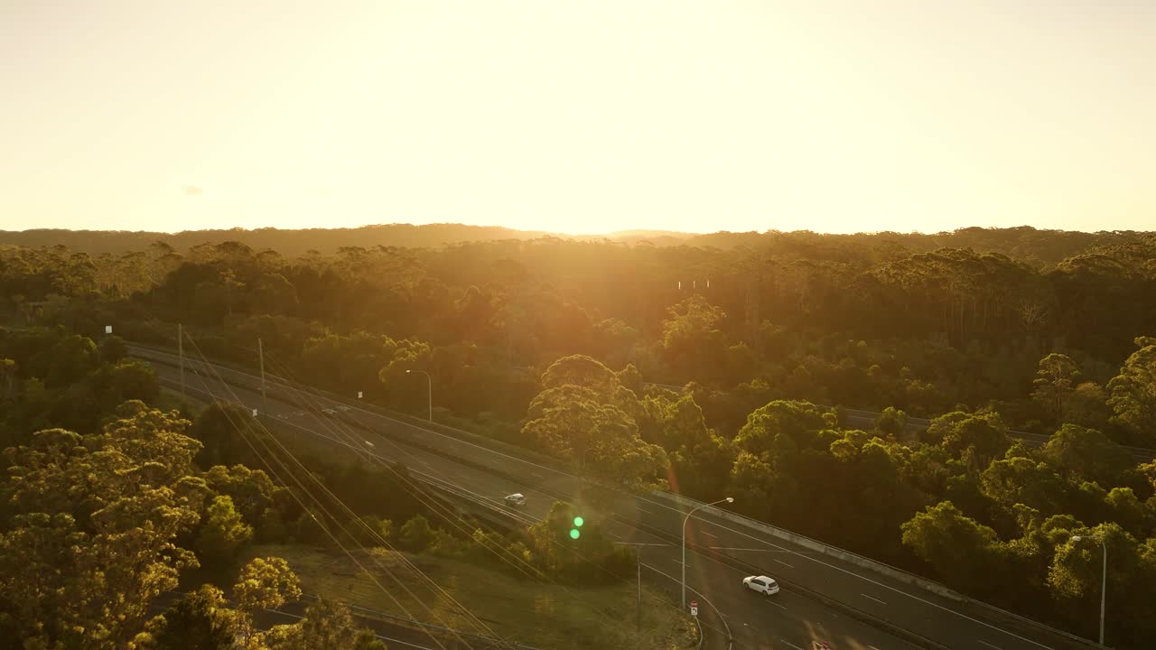 Golden hour light on the Illawarra Escarpment reveals lush ridges and forested valleys as cars drive through the green landscape at dusk