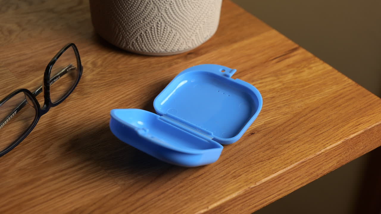 나무 탁자 위의 휴대용 케이스에 투명한 치아 보호대를 넣는 손