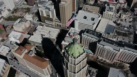 Toma-Aérea-De-Un-Dron-De-La-Bandera-Estadounidense-Ondeando-En-El-Viento-Sobre-San-Antonio,-Texas.