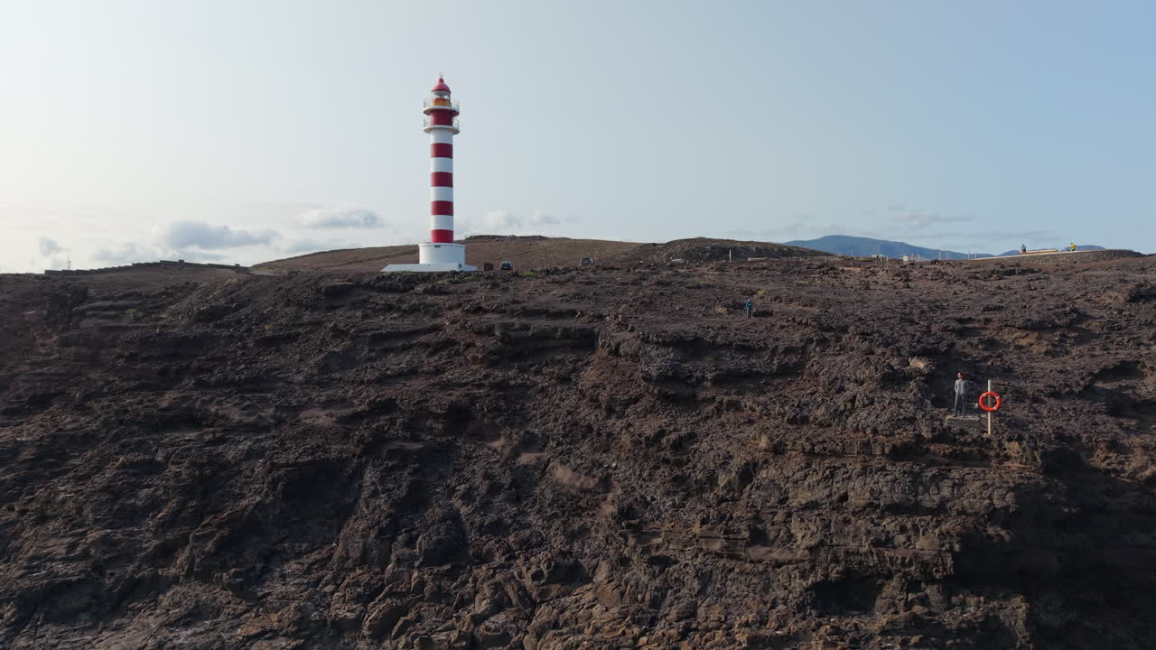 Coastal lighthouse perched on volcanic rocks, revealing dramatic aerial panorama of Punta Sardina in Gran Canaria's rugged seascape under clear summer sky