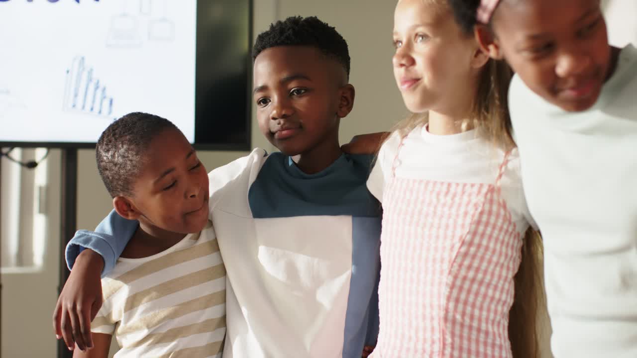 Vari bambini preadolescenti in piedi, uniti, appoggiati e sorridenti in un'aula davanti a uno schermo di presentazione.