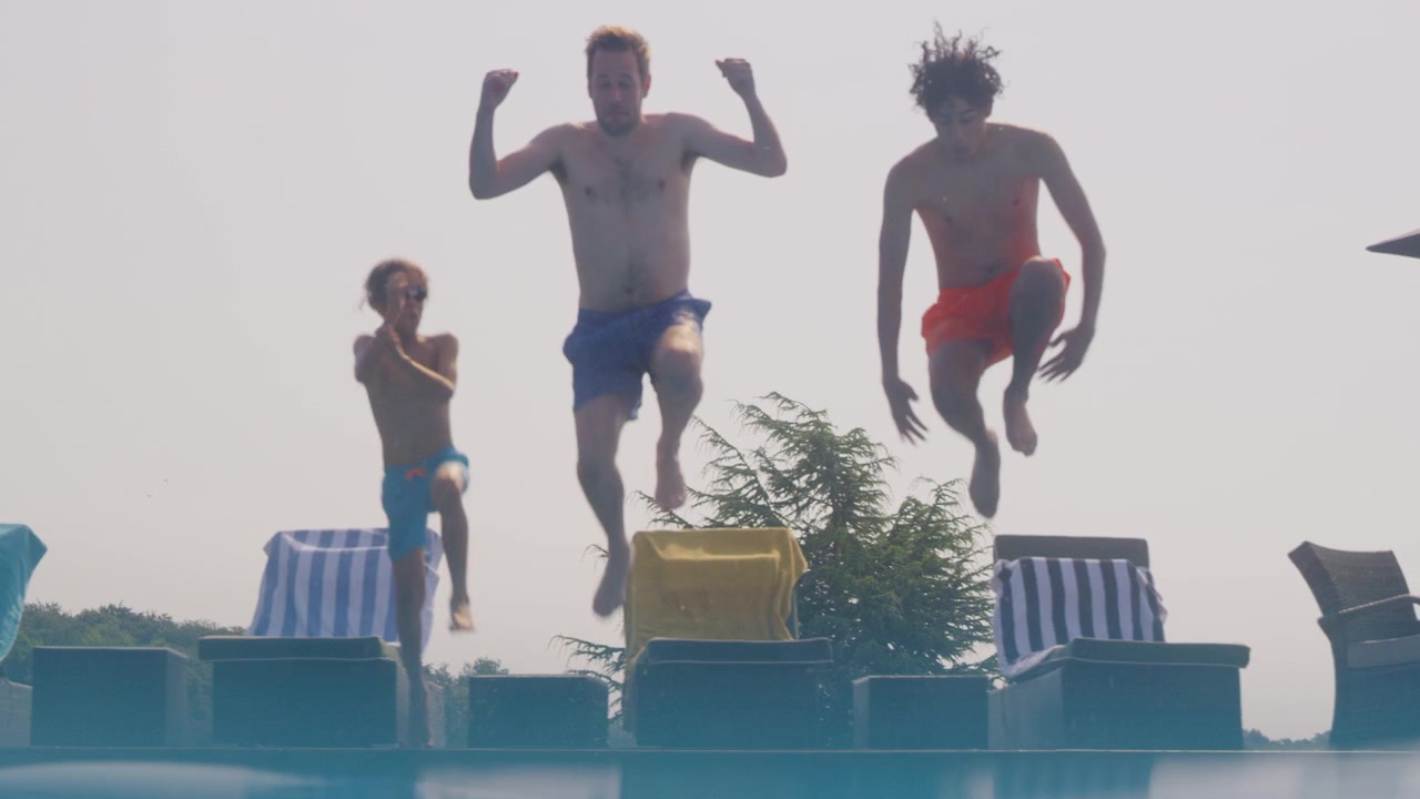 Ripresa subacquea di un padre che si tuffa in una piscina all'aperto con i figli durante le vacanze estive insieme.