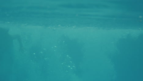 fotografía submarina de un padre saltando a la piscina al aire libre con sus hijos en vacaciones de verano juntos